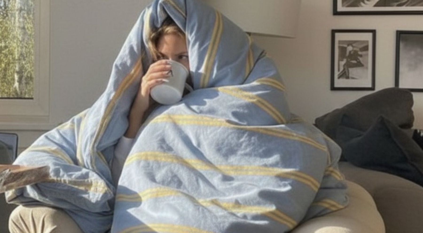 Good sleep hygiene habits of a woman sitting in a soffa covered with blue stripe sheet drinking from a cup